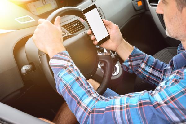 muž za volantom auta s mobilom v ruke