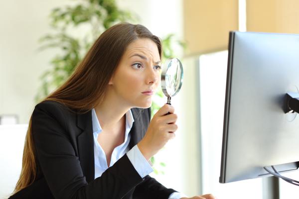 žena v práci pozerá cez lupu do monitora