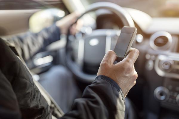 muž sediaci za volantom auta drží mobil v ruke